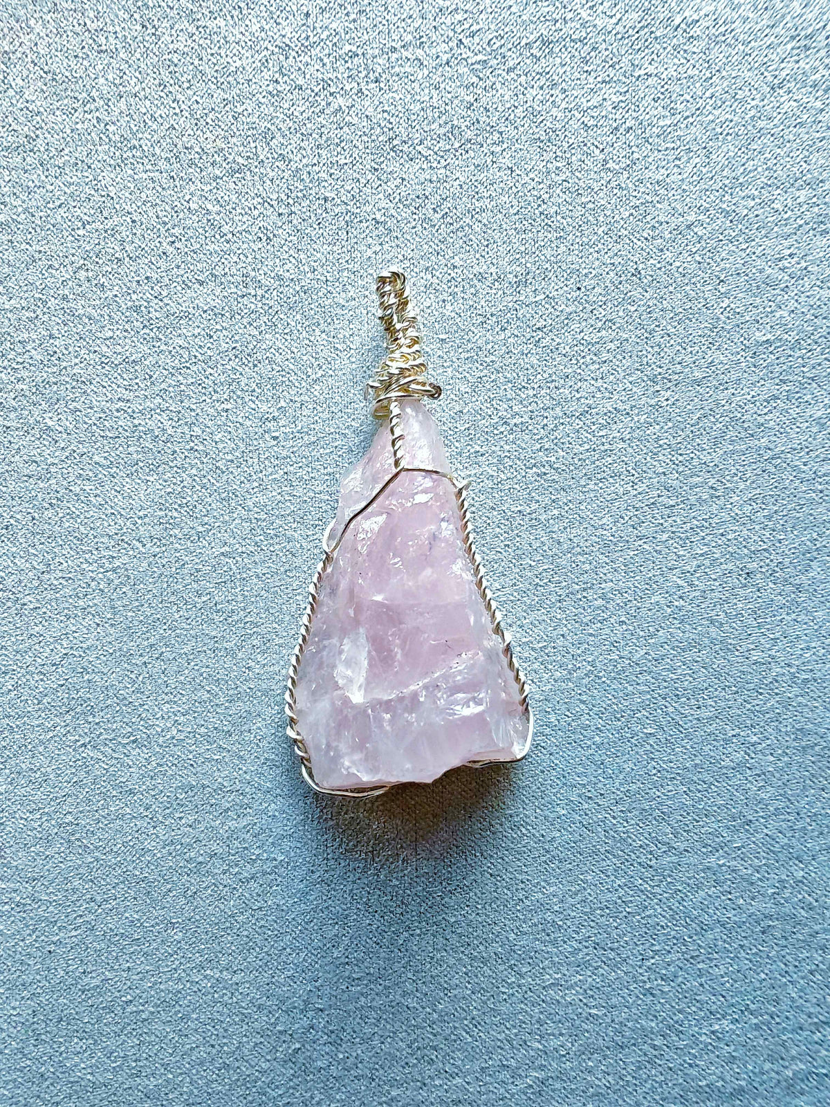 Colgante de cuarzo rosa alargado con vetas naturales, engarzado con hilo de cobre bañado en plata.