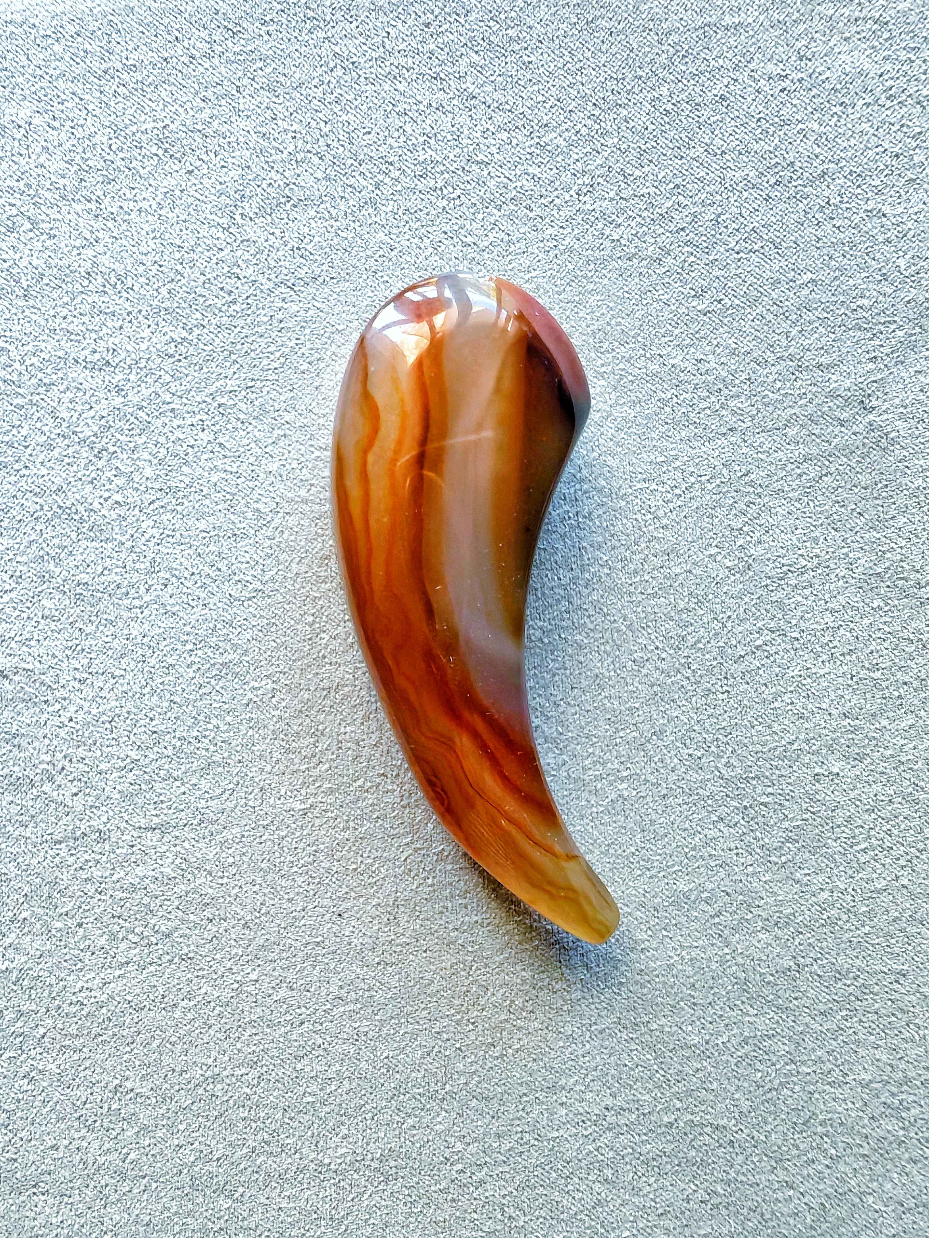 Cuerno de ágata pulido en tonos naranja, crema y marrón con vetas naturales, forma curva ideal como masajeador o colgante