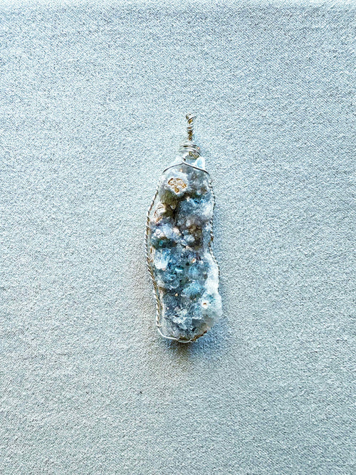 Colgante de drusa de amatista clara en tonos azul-gris engarzada a mano con hilo de cobre bañado en plata, con cordón negro incluido