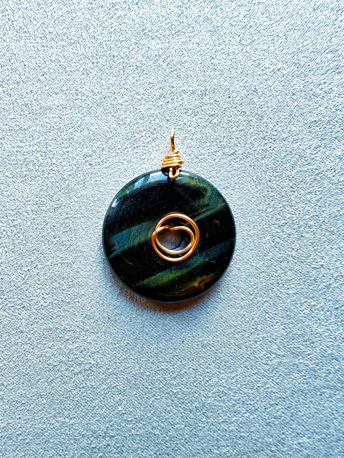 Colgante donut de ojo de halcón oscuro con bandas azuladas y verdosas y engarce de bronce en espiral