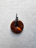 Colgante circular de ojo de tigre con vetas doradas y marrones y engarce de cobre en espiral