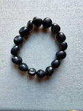 Pulsera de piezas negras redondeadas e irregulares de turmalina sobre fondo gris