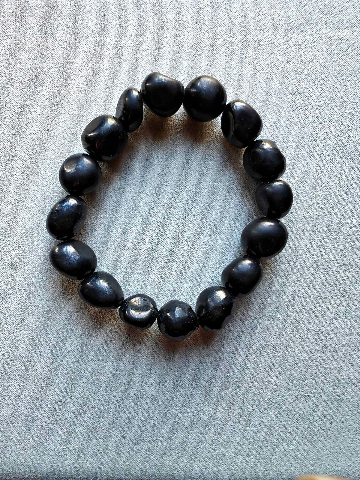 Pulsera de piezas negras redondeadas e irregulares de turmalina sobre fondo gris