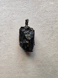 Colgante de turmalina negra bruta engarzado a mano con cobre bañado en acero negro, con cordón negro incluido