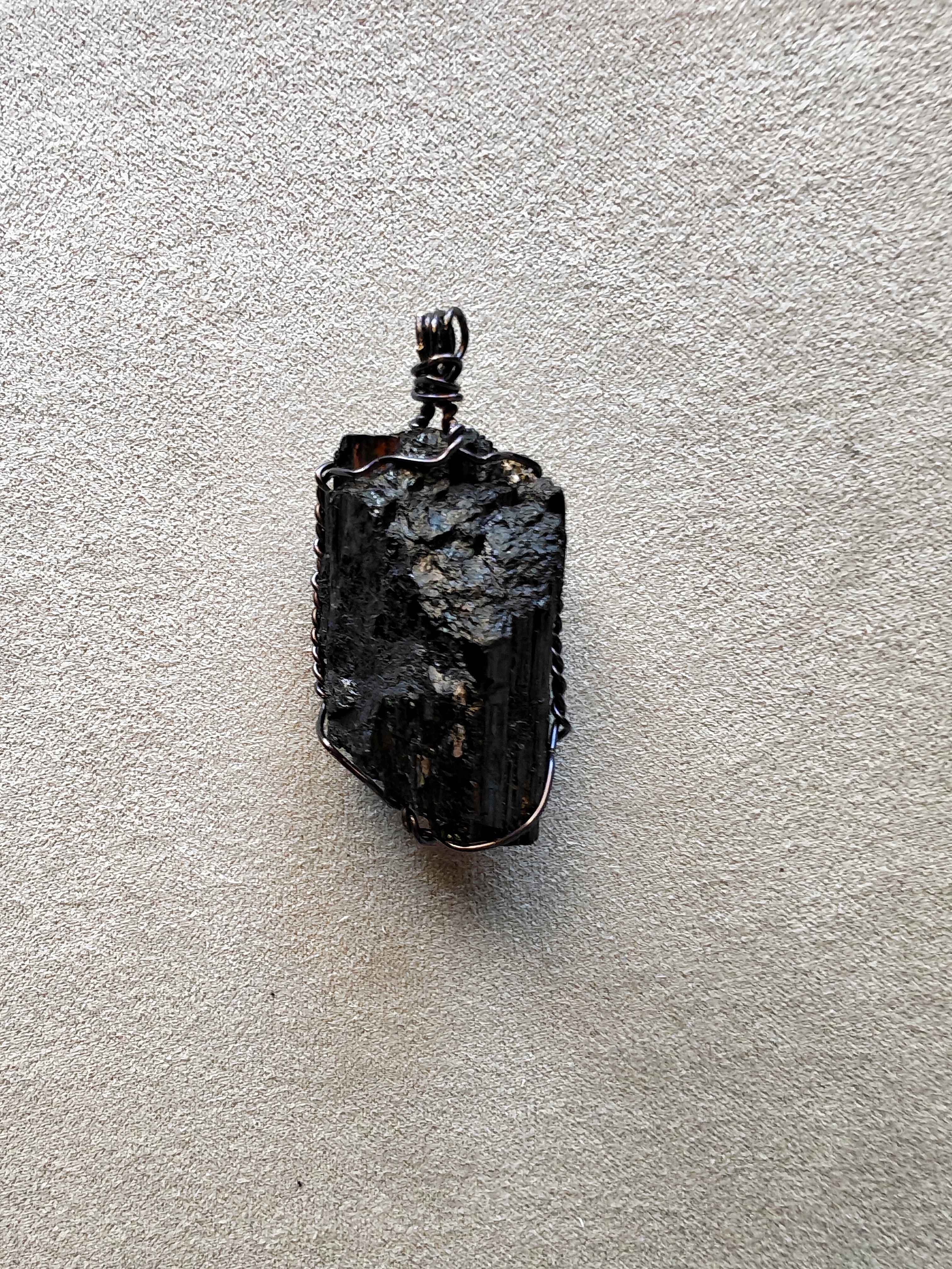 Colgante de turmalina negra bruta engarzado a mano con cobre bañado en acero negro, con cordón negro incluido