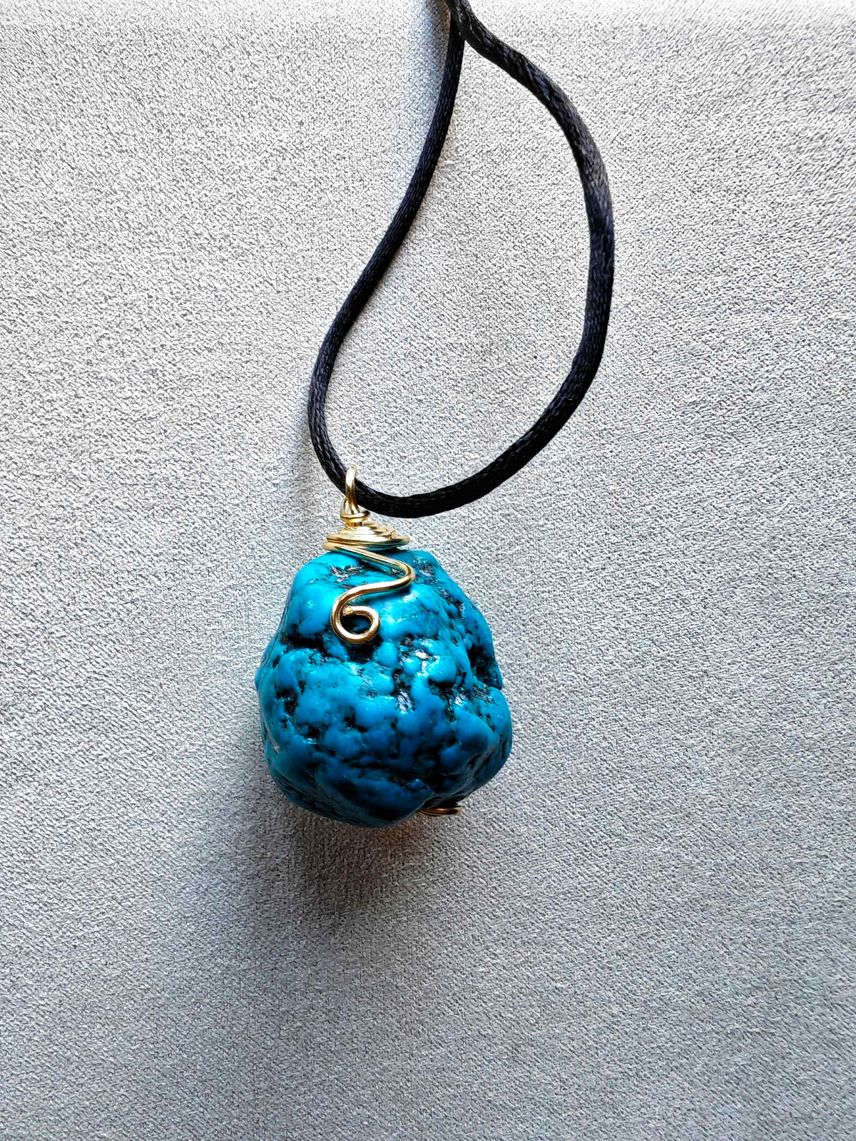 Colgante de turquesa azul de forma redondeada con vetas oscuras, engaste de hilo con detalle en espiral y cordón negro.